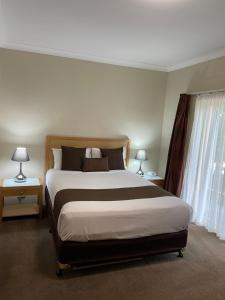 a hotel room with a bed, chair, and nightstand at Noah's Mid City Motor Inn Muswellbrook in Muswellbrook