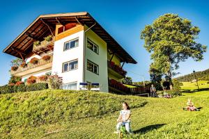 a little girl sitting in the grass in front of a house at Haus Lohengrin Ferienwohnung 1 in Siusi