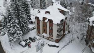 a building covered in snow with cars parked in the yard at Aber Apartmani Kopaonik in Kopaonik