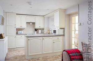 a white kitchen with white cabinets and a sink at Inglenook Cottage in Bourton on the Water