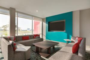 avid hotels - Chicago O Hare - Des Plaines في ديس بلينز: غرفة معيشة مع أريكة وتلفزيون على الحائط