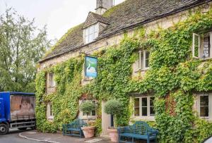 a building covered in ivy with blue chairs outside at Swan View in Southrop