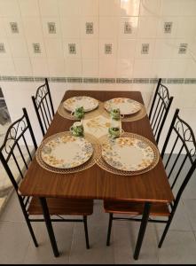 une table en bois avec quatre chaises et des assiettes. dans l'établissement Laguna Condo Resort Port Dickson, à Port Dickson