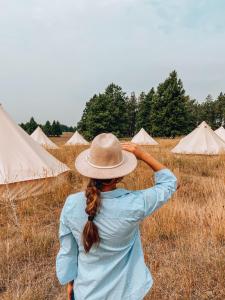 una mujer con un sombrero parada en un campo con tiendas de campaña en Wander Camp Glacier, en Coram