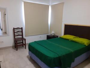 Un dormitorio con una cama verde y una silla en PARQUE LELOIR, ITUZAINGO en Villa Leloir
