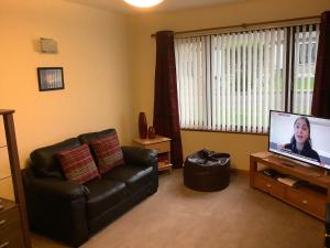 a living room with a black leather couch and a flat screen tv at 8 Jib Park, Finstown in Finstown