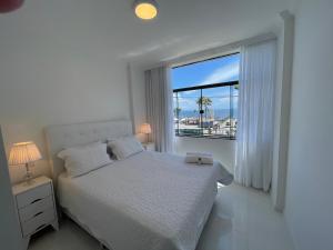 Dormitorio blanco con cama y ventana grande en SALVADOR Ondina 3 quartos frente praia en Salvador