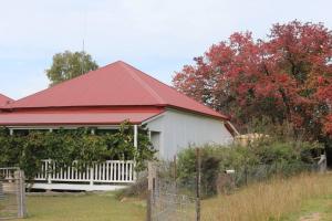 a white house with a red roof and a fence at Glenlyon Dam Holiday Cottage & Farmstay in Stanthorpe