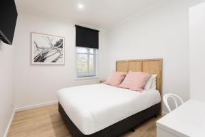 een slaapkamer met een wit bed met roze kussens bij Grand Terminus Hotel in Bairnsdale