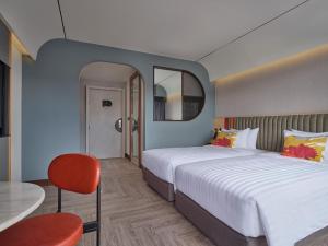 a hotel room with two beds and a red chair at The Quarter Onnut by UHG in Bangkok