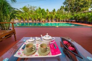 a tray with cups and tea pots on a table next to a pool at SaffronStays Adora Woods and Hills - 4BHK Murud Villa with Pool, Kids Pool & Beach Fun in Jambrung 