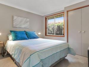 Un dormitorio con una cama con almohadas azules y una ventana en Cleveland Place, en Culburra Beach