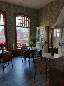 un comedor con mesas, sillas y ventanas en B&B Villa de Beuk, en Stadskanaal