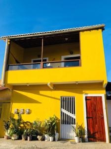 una casa gialla con una porta rossa e piante in vaso di Casa do Sol Flecheiras a Trairi