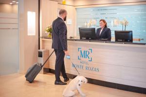 a man with a suitcase and a dog at a counter at Hotel Monte Rozas in Las Rozas de Madrid