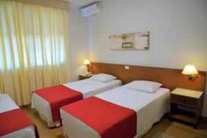 um quarto de hotel com duas camas com lençóis vermelhos e brancos em Hotel Majestic em Águas de Lindoia