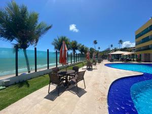 a pool with tables and chairs next to the ocean at Tabatinga Residence Flat Pé na Areia II in Conde