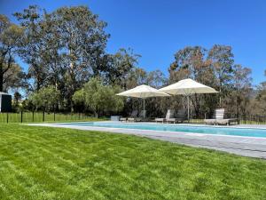 a swimming pool with two umbrellas and some grass at Wine Country Villas in Pokolbin