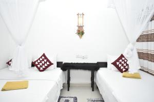 two beds in a room with white curtains and a table at Sigiri Rock Side Home Stay in Sigiriya