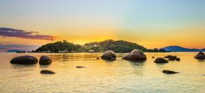 a group of rocks in the water at sunset at Pousada Casa do Oscar in Governador Celso Ramos