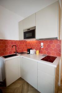 a kitchen with white cabinets and red tiles on the wall at Le Petit Marius in Aix-en-Provence
