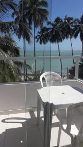 a white table and chair on a balcony with palm trees at Suíte em Japaratinga com Vista do Mar in Japaratinga