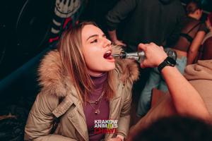 Een jonge vrouw drinkt uit een microfoon. bij Let's Rock Party Hostel in Krakau