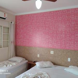 a bedroom with two beds and a pink wall at Raízes Hotel in Cajobi