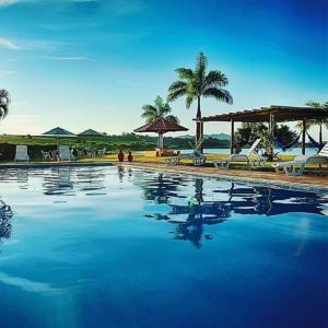 una piscina con agua azul, sillas y palmeras en Villa Interlagos de Minas, en Guapé
