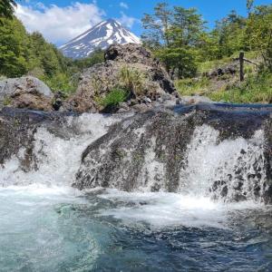 una cascata con una montagna innevata sullo sfondo di Vista al volcán con tinaja y río en Conguillío a Curacautín