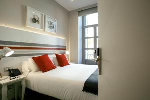 Un dormitorio con una cama blanca con almohadas rojas y una ventana en Legazpi Doce Rooms & Suites, en San Sebastián