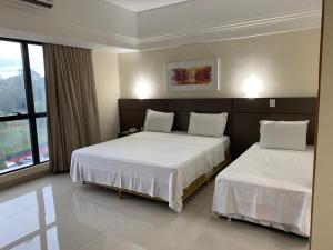 a bedroom with two beds and a large window at Tropical Executive Hotel flat in Manaus