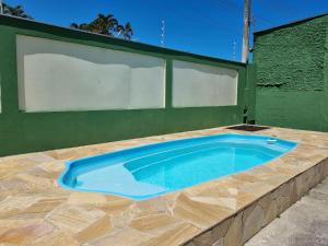 a swimming pool in front of a green wall at Acolhedora casa renovada - Piscina e a 100m da praia in Caraguatatuba