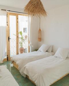 two beds in a white bedroom with a window at Blue Waves Boutique Hostel in Tamraght Ouzdar