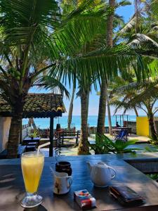 a glass of orange juice sitting on a table near the beach at Praneeth Guest House in Mirissa
