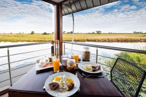 a table with plates of breakfast food and a view of a river at The Namushasha River Villa in Kongola