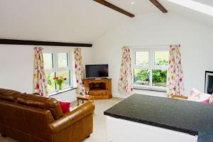 a living room with a couch and a tv and two windows at Greenswood Cottage - Cosy cottage, rural location, beautiful landscaped gardens with pond and lake in Dartmouth