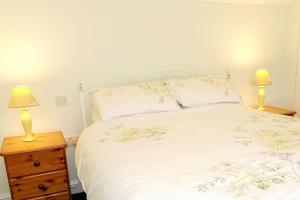 a bedroom with a bed with two lamps on a night stand at Greenswood Cottage - Cosy cottage, rural location, beautiful landscaped gardens with pond and lake in Dartmouth