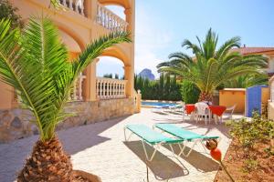 a patio with chairs and tables and palm trees at Villa Senieta - PlusHolidays in Calpe