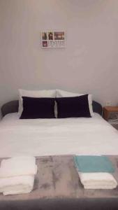 Una cama blanca con almohadas negras y toallas. en ORA-PRN,cosy apartment in the city center en Pristina
