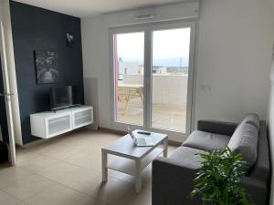 uma sala de estar com um sofá, uma mesa e uma televisão em Charmant T2 avec grande terrasse au calme em Saint-Jean-de-Védas