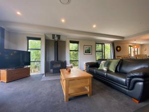 a living room with a black leather couch and a television at 3 Oakview Close in Hanmer Springs