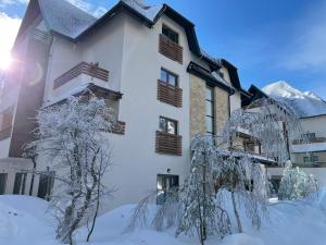 a building covered in snow with trees in the foreground at Apartman Pinewood Divcibare in Divčibare
