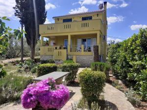 a yellow house with a bench and purple flowers at Apartment Brane - charming and close to the sea in Sutomišćica