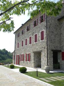 un gran edificio de piedra con ventanas de contraventanas rojas en Agriturismo Althea, en Vittorio Veneto