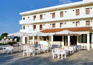 un bâtiment avec des tables, des chaises blanches et des parasols dans l'établissement Hotel Prassino Nissi, à Moraitika