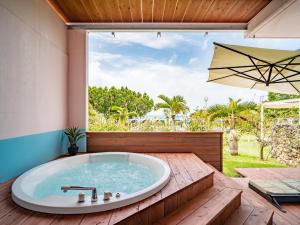 eine Whirlpool-Badewanne in einer Terrasse mit Sonnenschirm in der Unterkunft ザ・ビーチテラスホテルアオ石垣 in Ishigaki-jima