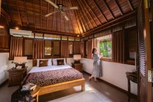 a woman standing in a bedroom looking out the window at Nur Guest House by Purely in Ubud