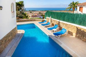 uma piscina com cadeiras azuis e o oceano em Villa Proa em Son Bou