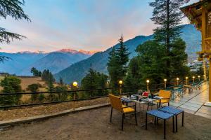 a table and chairs on a balcony with a view of mountains at The Hosteller Shangarh, Sainj Valley in Sainj